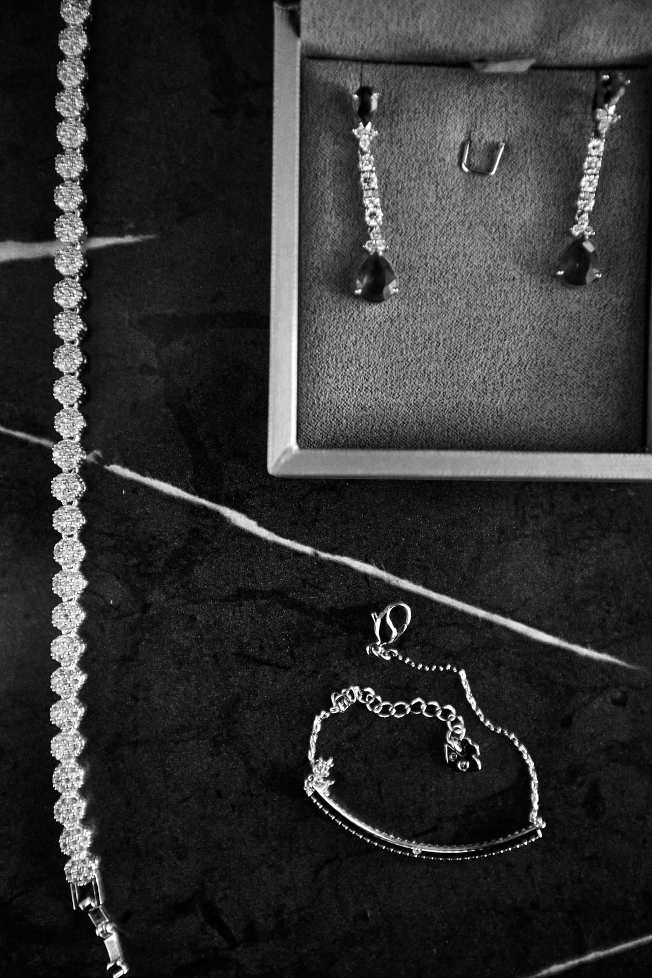 Joias sobre mármore escuro: pulseira de cristais, brinco pendente em estojo e pulseira fina